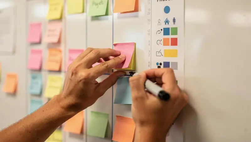 Une main déplace un post-it sur un tableau de planification en colonnes