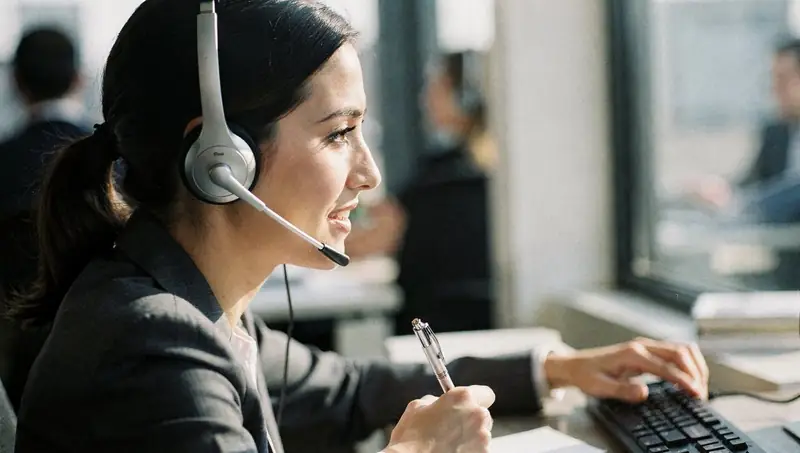 Une conseillère clientèle avec un casque prend des notes pendant un appel