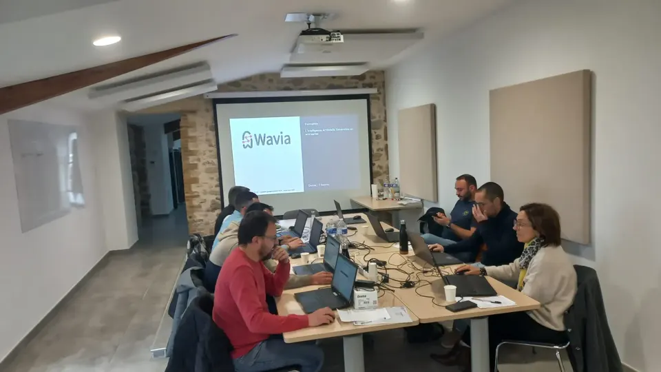 Atelier de formation IA : une petite équipe travaille sur ordinateurs portables devant l'écran de présentation Wavia