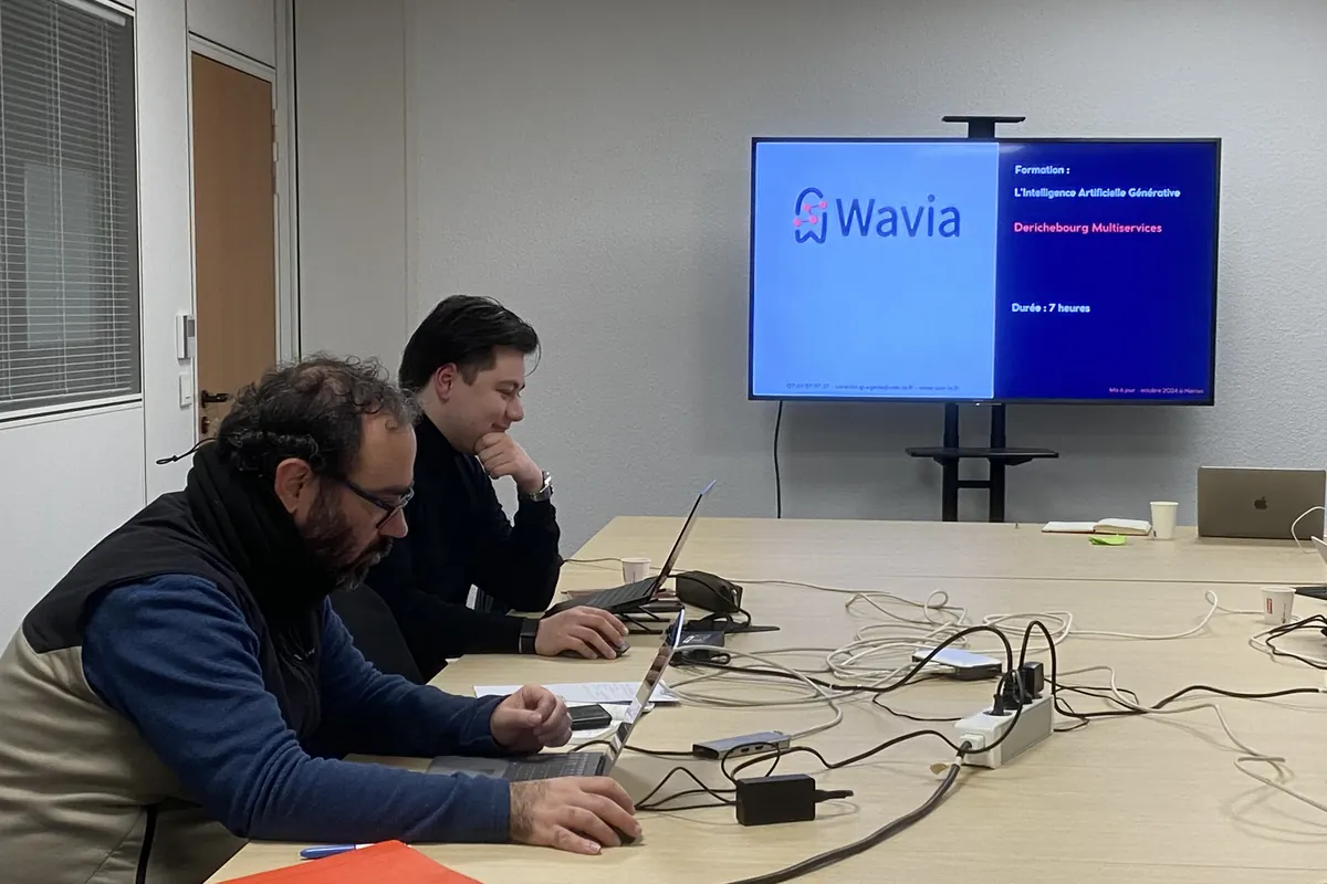 Deux participants travaillent sur leur ordinateur pendant une formation Wavia en entreprise, le support de la journée affiché à l'écran
